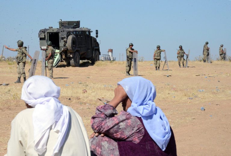 Turkish soldiers stand guard as people from the Syrian town of Ayn al-Arab or Kobani, in the background, wait to cross into Turkey following the attacks by IS militants as seen from the Turkish side of the border in Suruc, Turkey, Friday, June 26, 2015. (AP Photo)