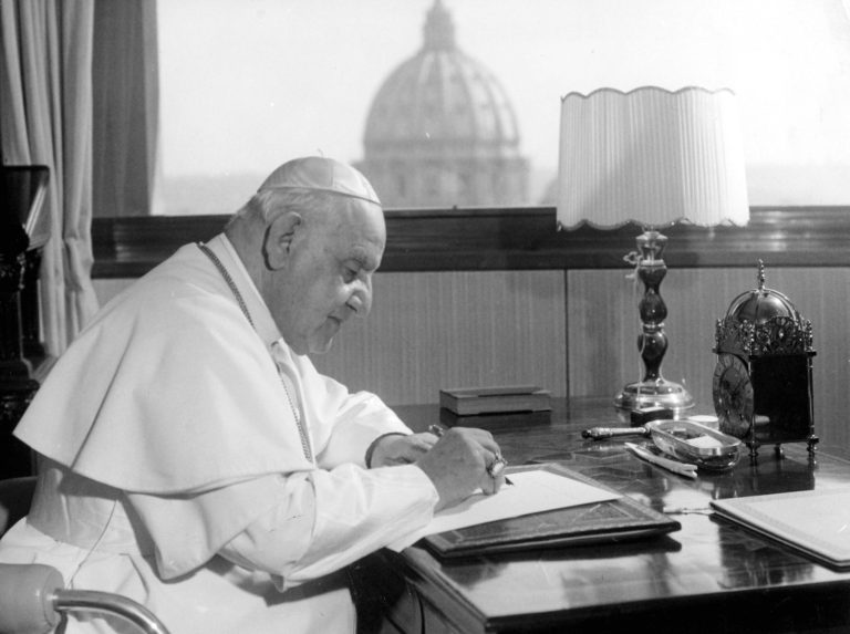 FILE - In this April 15, 1963 file photo, Pope John XXIII sits at his working desk in his studio in a IX century tower in the Vatican gardens. In background the dome of St. Peter's Basilica. The Pontiff found the tower - once a fortress and later the Vatican observatory - abandoned and in decay. He liked it, particularly for the beautiful view from its covered terrace, embracing a great part of Rome and the surrounding country, in clear weather as far as the sea, distant about 25 kilometers (16 miles). He had it repaired and spends many days working in the studio he has had arranged there. While much of the focus of Sunday's dual canonization will be on Pope John Paul II's globe-trotting, 26-year papacy and his near-record sprint to sainthood, many older Catholics will be celebrating the short but historic pontificate of the 