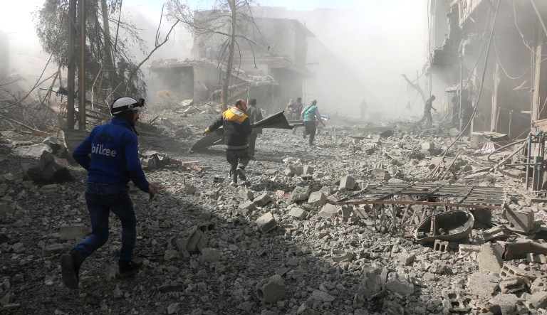 In this photo released on Tuesday Feb. 20, 2018 which provided by the Syrian Civil Defense group known as the White Helmets, shows members of the Syrian Civil Defense run to help survivors from a street that attacked by airstrikes and shelling of the Syrian government forces, in Ghouta, a suburb of Damascus, Syria. A Syrian monitoring group and paramedics say government shelling and airstrikes on rebel-held suburbs of the capital, Damascus, killed at least 98 people on Monday. (Syrian Civil Defense White Helmets via AP)