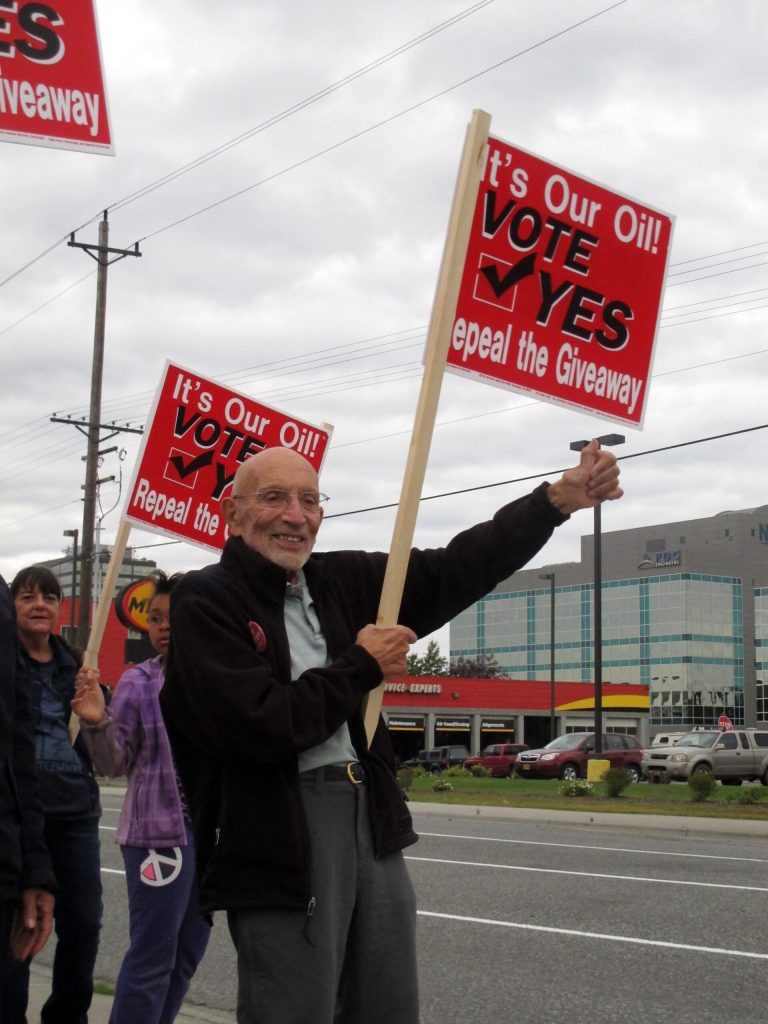 FILE - In this Aug. 8, 2014 file photo, Vic Fischer, a leader of the effort to repeal the oil tax system passed by Alaska state lawmakers in 2013, takes part in a sign-waving event on a busy street in Anchorage, Alaska. Alaskans head to the polls Tuesday, Aug. 19, 2014, to decide if the state's old system for taxing oil companies, passed in 2007 after some lawmakers were suspected of bribery, is better than the new system, a tax cut passed last year to try to attract investment from petroleum companies. (AP Photo/Becky Bohrer, File)