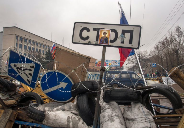 Russian national flags fly above barricades with a road sign 