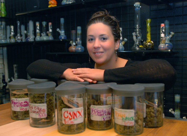 Danielle Baldwin shows off strains of medical marijuana Thursday, Oct. 2, 2014, kept at Puffs Smoke Shop in Ashland, Ore., which is seeking a license as a medical marijuana dispensary. The city of Ashland is one of more than a dozen around Oregon that have imposed or are planning to impose a tax on marijuana if voters legalize it in November 2014. Though the measure prohibits anyone but the state from taxing marijuana, the cities hope by enacting a tax before the voters decide, their taxes will be grandfathered in. (AP Photo/Jeff Barnard)