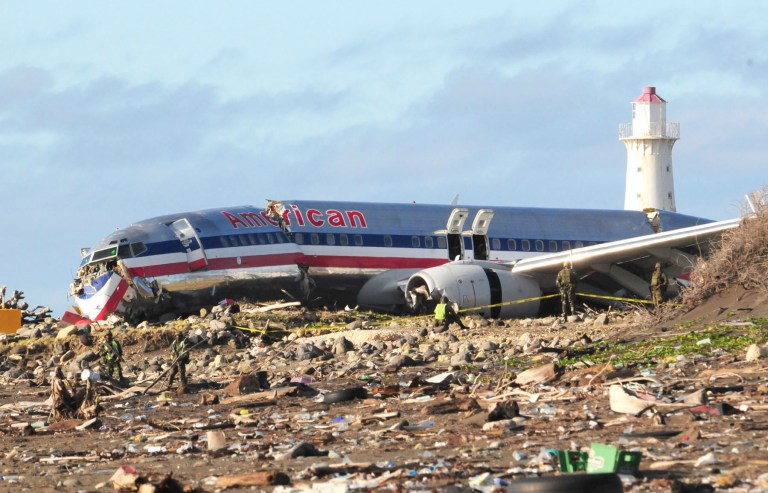 FILE - In this Dec. 23, 2009, file photo, workers sift through debris surrounding the fuselage of American Airlines flight AA331 which crash landed overnight on a flight from Miami to Jamaica, just beyond the runway of Norman Manley International Airport, in Kingston Jamaica. An investigation into a plane accident almost five years ago at a Jamaican airport has concluded that an American Airlines jet flying in from Miami botched the landing and the flight crew may have been fatigued. (AP Photo/Lloyd Robinson, File)   JAMAICA OUT