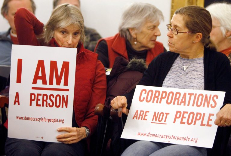 In this Jan. 20, 2012  photo, people hold signs during a gathering on the anniversary of the Citizens United decision in Montpelier, Vt. First, it was the Vermont senator with socialist leanings. Then it was Jerry of Ben & Jerry's ice cream fame. Now there are about 50 Vermont communities ready to chime in on a proposal to pass a Constitutional amendment to clarify that corporations do not have the same rights as human beings., (AP Photo/Toby Talbot)
