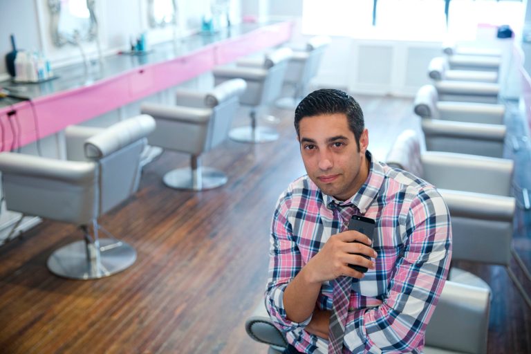 In this May 19, 2014 photo, Avi Shenkar, owner of Blo/Out Blow Dry Bars, poses for a photograph with his iPhone, in Philadelphia. Smartphones have become vital for on-the-go entrepreneurs such as Shenkar who runs his four hair salons from the palm of his hand. (AP Photo/Matt Rourke)
