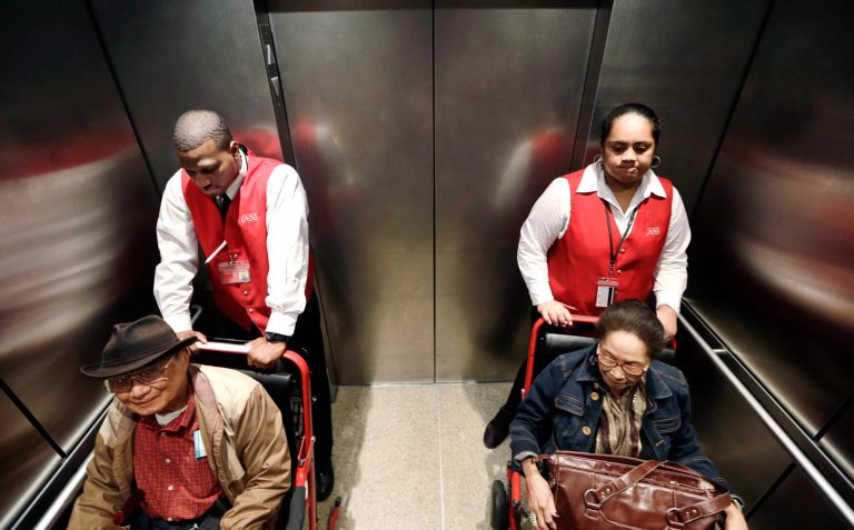 Wheelchair attendants Erick Conley, left, and Sesilia Vaitele assist a pair of passengers heading to an overseas flight at Seattle-Tacoma International Airport, in SeaTac, Wash. (AP/Elaine Thompson)