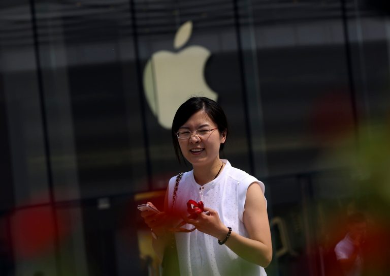 In this Sept. 5, 2014 photo, a Chinese woman holds an iPhone walks past an Apple store in Beijing, China. China's phone regulator said Tuesday, Sept. 30,  it has approved Apple Inc.'s iPhone 6 for use on Chinese networks after the company promised never to allow other governments access to users' information. Apple said sales start on Oct. 17. (AP Photo/Andy Wong)