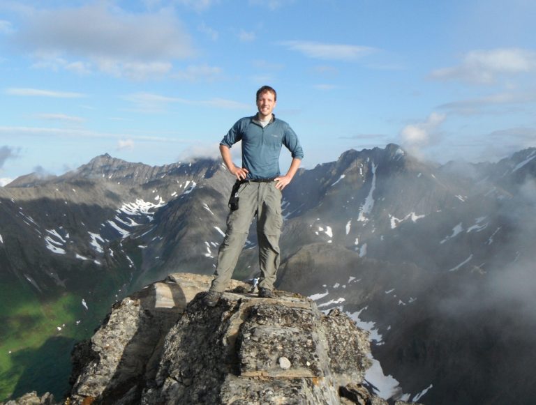   RETRANSMISSION TO CORRECT LOCATION - In this photo taken in July 2011, bear mauling victim Ben Radakovich stands in front of some peaks south of Anchorage, Alaska, that he was hoping to climb before the attack by the grizzly Sunday left him with a shredded back and neck lacerations. The 30-year-old resident of the Anchorage, Alaska, suburb of Eagle River was rescued almost two hours after he scrambled 30 feet up a tree. (AP Photo/Jason Hlasny)  