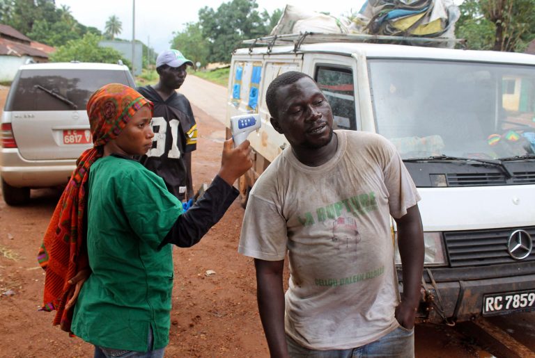 In this photo taken on Sunday, Sept. 7, 2014, a health worker, left, uses a thermometer to screen a man at a makeshift road block run by Guinean security forces outside the town of Forecariah, Guinea. Doctors Without Borders shuttered one of its Ebola treatment centers in Guinea in May. They thought the deadly virus was being contained there. The resurgence of the disease in a place where doctors thought they had it beat shows how history's largest Ebola outbreak has spun out of control. (AP Photo/Youssouf Bah)