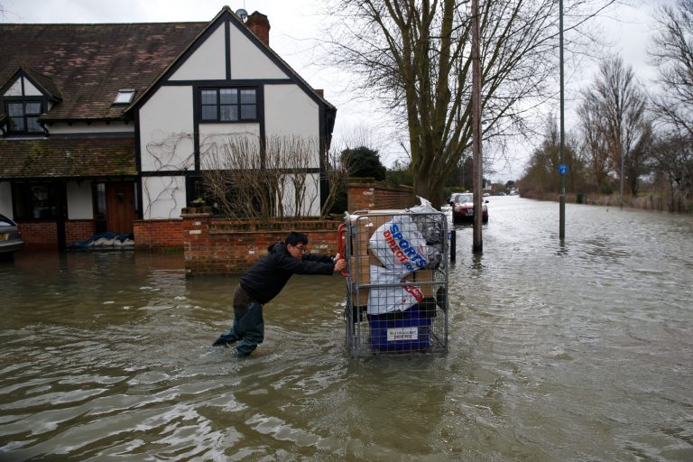 A local resident pushes belongings on a cart through the flooded part of the town of Staines-upon-Thames, England, as a police van patrols the area, Wednesday, Feb. 12, 2014. Prime Minister David Cameron insisted Tuesday that money is no object in the battle against the widespread flooding that has engulfed parts of England. Canceling a visit to the Middle East to oversee flood-fighting efforts, he told journalists that 