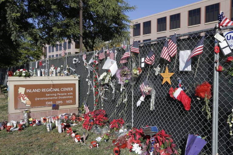 In this Tuesday, Dec. 29, 2015, photo, flowers and American flags honoring the victims of the attack on Dec. 2 are placed outside the Inland Regional Center where the fatal shooting took place in San Bernardino, Calif. At the IRC, Christmas never came. The staff was still gearing up for the holidays on Dec. 2, the day 14 people were massacred on the center's gleaming campus. (AP Photo/ Nick Ut)
