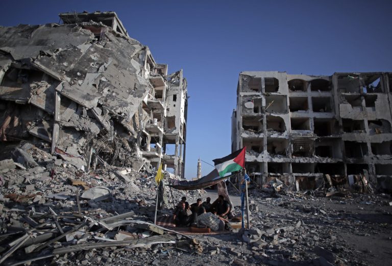 Palestinian Ziad Rizk, 38, sits with others in a shelter made of a blanket stretched over four boles next to one of the destroyed Nada Towers, where he lost his apartment and clothes shop, in the town of Beit Lahiya, northern Gaza Strip, Monday, Aug. 11, 2014. (AP Photo/Khalil Hamra)