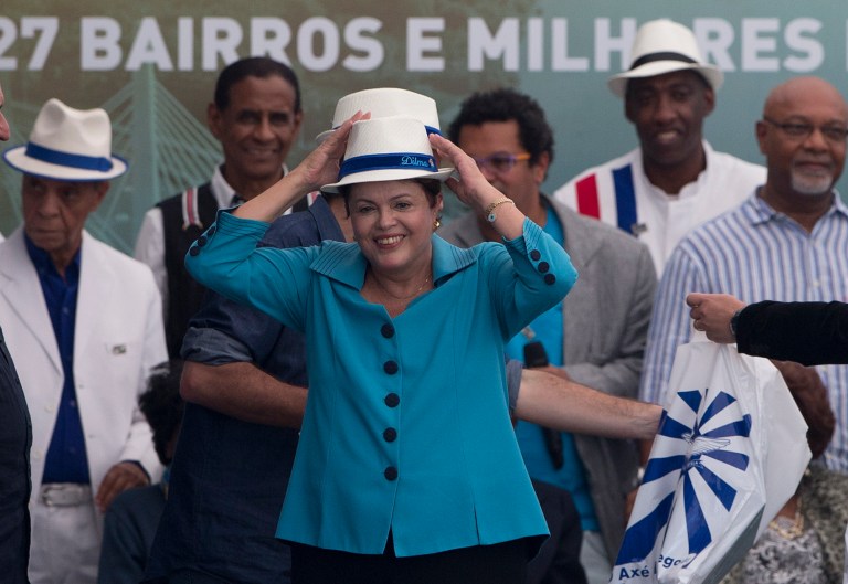 Brazil's President Dilma Rousseff, center, puts a hat during the inauguration of the BRT Transcarioca (Rapid Transit Bus) in Rio de Janeiro, Brazil, Sunday, June 1, 2014. The corridor has 39 kilometers long, cutting through 27 neighborhoods and will serve 320 thousand people every day, reducing in 60 per cent the average time of the commute. The corridor will connect the International Airport to the subway, which takes the passengers to the Maracana stadium. (AP Photo/Silvia Izquierdo)