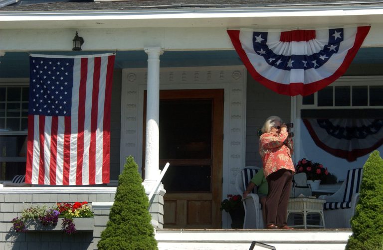 A woman stands on the porch of the Arundel Inn, across the street from the Bush compound, and looks through binoculars June 30, 2007 in Kennebunkport, Maine. (Photo by Darren McCollester/Getty Images)