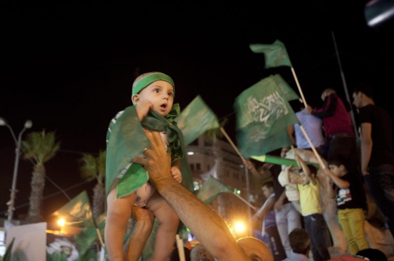 A Palestinian Hamas supporter holds up a little girl wearing green flags as people gather in the streets during celebrations for the cease-fire between Palestinians and Israelis, in the West bank city of Ramallah, Tuesday, Aug. 26, 2014.  Israel and Hamas agreed Tuesday to an open-ended cease-fire, halting a seven-week war that killed more than 2,200 people, the vast majority Palestinians, left tens of thousands in Gaza homeless and devastated entire neighborhoods in the blockaded territory. (AP Photo/Majdi Mohammed)