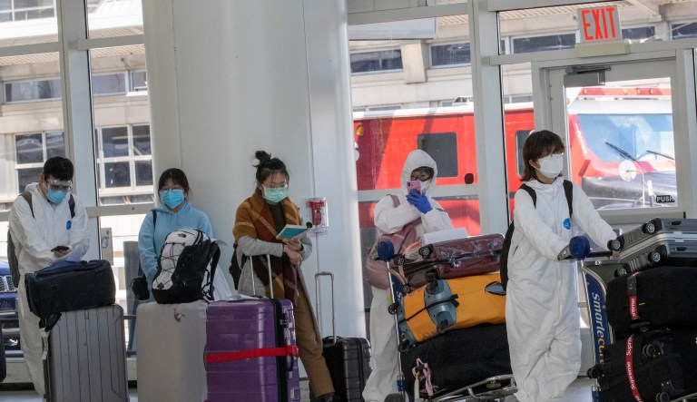 Passengers wear face masks and jumpsuits to fend off coronavirus as they wait in line to check in for their flights, Tuesday, March 24, 2020, at JFK airport in New York. 