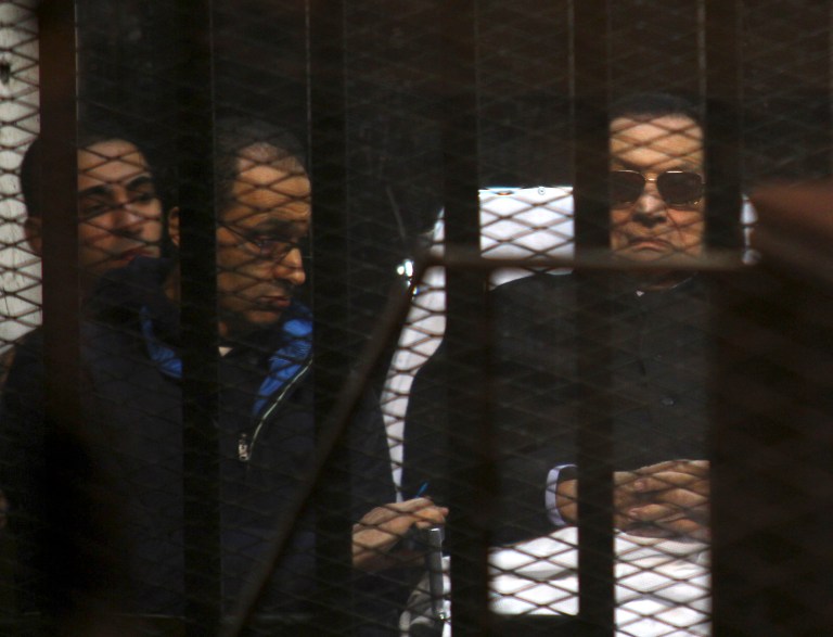 Ousted Egyptian President Hosni Mubarak, 86, lies on a gurney, next to his son Gamal, second left, in the defendants cage, during a court hearing in Cairo, Egypt, Saturday, Nov. 29, 2014. (AP Photo/Tarek el-Gabbas)