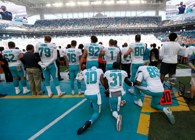 Miami Dolphins wide receiver Kenny Stills (10), free safety Michael Thomas (31) and tight end Julius Thomas (89), kneel during the National Anthem behind their teammates before an NFL football game against the Tampa Bay Buccaneers, Sunday, Nov. 19, 2017, in Miami Gardens, Fla. (AP Photo/Wilfredo Lee)