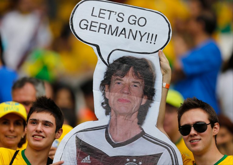 Brazil supporters hold a poster depicting Rolling Stones singer Mick Jagger wearing a Germany shirt prior to the World Cup semifinal soccer match between Brazil and Germany at the Mineirao Stadium in Belo Horizonte, Brazil, Tuesday, July 8, 2014. (AP Photo/Frank Augstein)