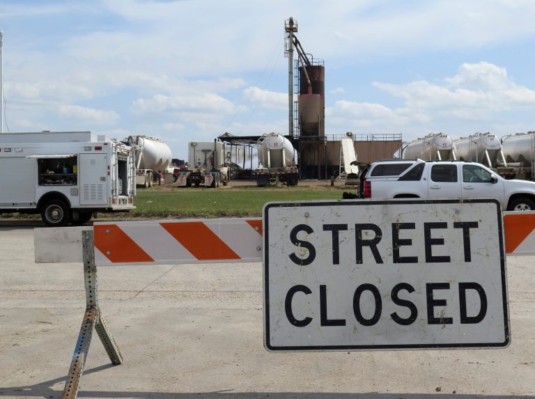 In this Wednesday, July 23, 2014 photo, a street is closed off in front of the an oil field supply company facility in Williston, N.D. that was hit by a fire. Officials say the fire started about midnight Monday and burned most of Tuesday. At its height, the blaze sent fireballs hundreds of feet into the air. No one was injured or killed. A more efficient system must be established to alert residents of danger in North Dakota's booming oil patch, an emergency manager and residents said, after authorities failed to alert the public for more than six hours when the facility storing toxic chemicals exploded. (AP Photo/Josh Wood)