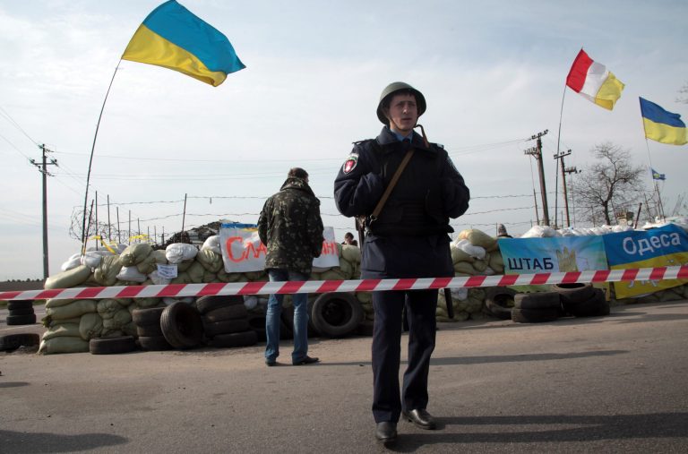 A Ukrainian police officer stands guard at a checkpoint, with Ukrainian flags, that was attacked by unknown men outside the Black Sea port of Odessa, Ukraine, Friday, April 25, 2014. In southeastern Ukraine, seven people were injured early Friday by a blast at a checkpoint set up by local authorities and pro-Ukraine activists outside the Black Sea port of Odessa. Local police spokesman Volodymyr Shablienko said unknown men had thrown a grenade at the checkpoint. The Odessa region has so far not been affected by the pro-Russian insurgency. (AP Photo/Sergei Poliakov)