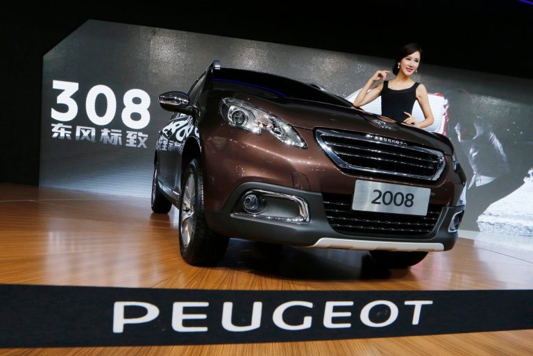 In this Nov. 21, 2013 photo, a model poses besides a Peugeot 2008 in front of the screen reads 
