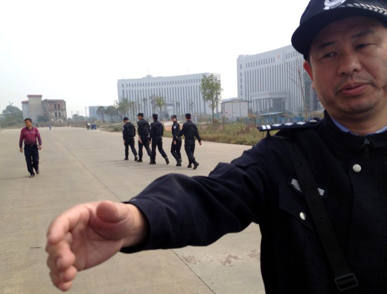FILE - In this Oct. 28, 2013 file photo, a Chinese police officer reaches out towards a journalist outside the courthouse where a trial of Chinese activists from a group that urges fellow citizens to embrace their constitutional rights is underway in Xinyu city in eastern China's Jiangxi province. A court in eastern China has imposed jail terms of up to six and a half years to three activists who were part of a nascent civil rights movement that has urged government officials to publicly disclose their assets. Attorney Zhou Ze says a district court in the city of Xinyu on Thursday, June 19, 2014 sentenced activists Liu Ping and Wei Zhongping to six and a half years' imprisonment each while another activist, Li Sihua, was handed three years. (AP Photo/Aritz Parra, File)