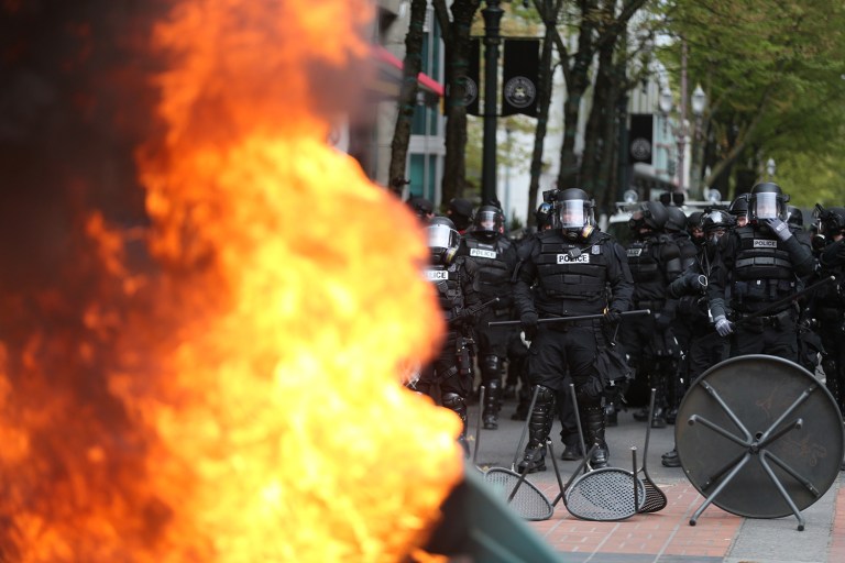 Police officers make a formation near a fire during a May Day rally in downtown Portland, Ore., Monday, May 1, 2017. Police in Portland said the permit obtained for the May Day rally and march there was canceled as some marchers began throwing projectiles at officers. (Dave Killen/The Oregonian via AP)