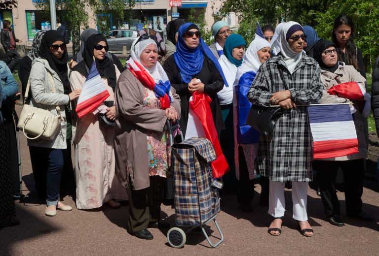 Woman wearing  traditional muslim scarf and holding French flags gather outside the town hall in Mantes la Ville, north west of Paris, Friday, May 16, 2014, in protest of the ban of a new mosque. A new mosque for Muslims approved last year and paid with a heavy deposit is suddenly in limbo in a town outside Paris, and new shops in a southern town that reflect Muslims' traditions will be banned. Newly-installed far-right mayors in Mantes-la-Ville, west of the French capital, and in Beaucaire, in southwest France, are rolling out their programs and the large Muslim populations in their towns risk getting crushed. (AP Photo/Michel Euler)