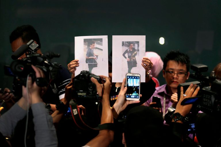 FILE - In this March 11, 2014 file photo, members of the media scramble with their smart phones and cameras to photograph pictures of the two men, a 19-year-old Iranian identified by Malaysian police as Pouria Nour Mohammad Mehrdad, left, and the man on the right, his identity still not released, who boarded the missing Malaysia Airlines jet MH370 with a stolen passports, held up by a Malaysian policewoman during a press conference,  in Sepang, Malaysia. News early on that two of the 239 passengers on board used stolen passports fueled speculation of terrorism. However, Malaysian police determined that the men were Iranians seeking to illegally migrate to Europe and not terrorists.   (AP Photo/Wong Maye-E, File)