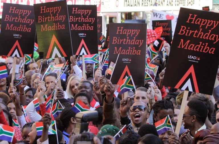   In this photo taken Friday June 1, 2012, members of the public and celebrities gather to videotape a sing-a-long birthday wish for former president Nelson Mandela, portrait on woman's shirt, on Nelson Mandela Square in Johannesburg. Mandela's office on Monday June 18 2012 has released the video of South Africans singing 