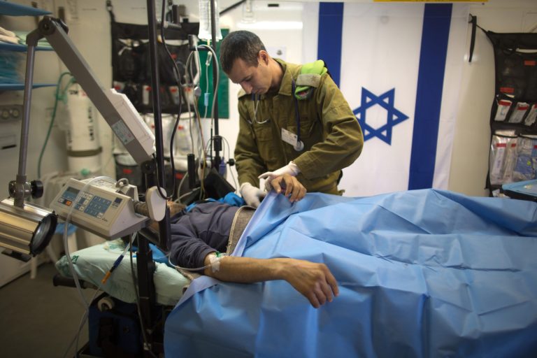 Israeli military medic tends  a Syrian man who was wounded in the ongoing violence in Syria, in a military hospital located in the Golan Heights near the border with Syria on Tuesday, Feb. 18, 2014. Since the Syrian conflict erupted almost three years ago hundreds of Syrians have received treatment in Israeli hospitals.(AP Photo/Menahem Kahana, Pool)