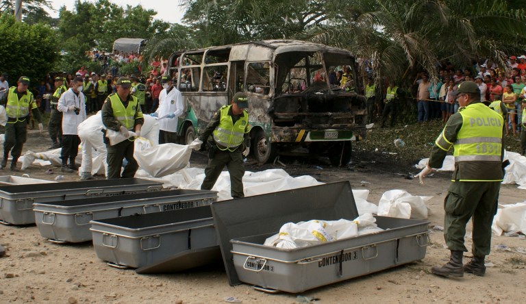 Police carry bags with the remains of children who burned to death in a bus, behind, in Fundacion in northern Colombia, Sunday, May 18, 2014. Colombian authorities have detained the driver of the overcrowded bus that burned, killing 32 children, the local mayor said Monday. Luz Estella Duran, mayor of the village of Fundacion, said witness accounts suggest the driver may have left the vehicle running with the children on board when he descended from the bus to fill tank from a portable gas container. (AP Photo/Oscar Mejia, Hoy Diario del Magdalena)