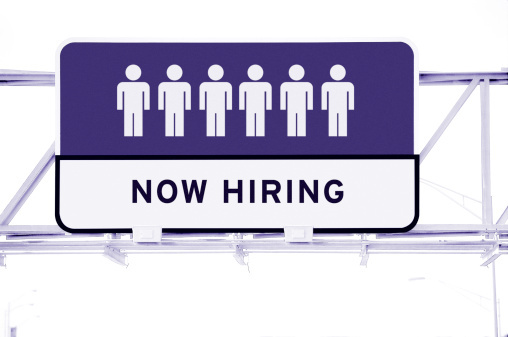 low angle view of an overhead road sign saying now hiring