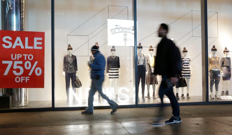 Pedestrians pass an H&M storefront window advertising discounts up to 75 percent in New York on Jan. 14, 2014.