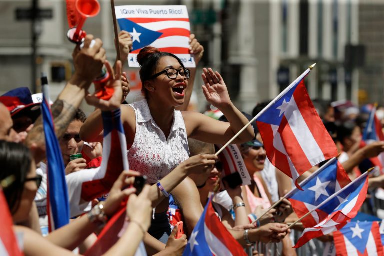 People cheer and wave flags during the National Puerto Rican Day Parade in New York, Sunday, June 8, 2014. The annual parade features thousands of participants in colorful costumes, along with floats and music, and of course, throngs of onlookers. (AP Photo/Seth Wenig)