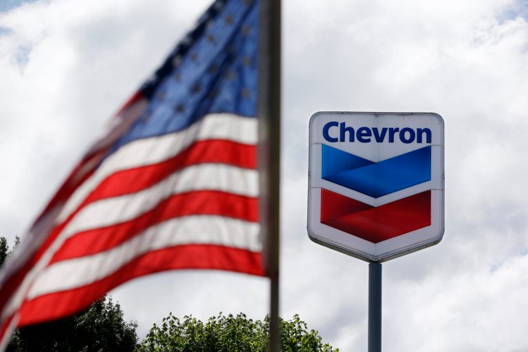 In this May 23, 2013, file photo, a U.S. flag flies in view of a Chevron gas station in Blaine, Washington. Chevron reports quarterly earnings on Friday, Jan. 31, 2014.