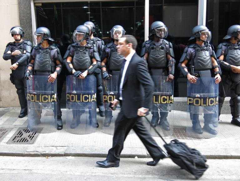A pedestrian walks by a line of police officers as they block the entrance of the Transportation Department when subway workers arrive to request a meeting with officials, to negotiate better salaries and benefits in Sao Paulo, Brazil, Monday, June 9, 2014. Striking subway workers clashed in a central commuter station Monday while union leaders threatened to maintain the work stoppage through the World Cup's opening match in Sao Paulo this week. (AP Photo/Adriana Gomez Licon)