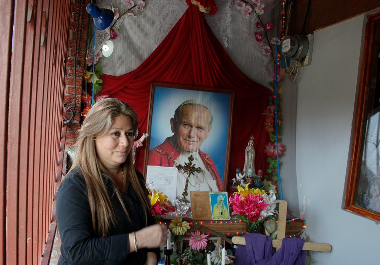 FILE - In this July 5, 2013 file photo, Floribeth Mora stands by her shrine to Pope John Paul II inside the entrance to her home in La Union de Cartago, Costa Rica. Mora, her doctors and the Catholic Church say her aneurysm disappeared in May of 2011 in a miracle that cleared the way for the late pope to be declared a saint. Mora will attend the ceremony at the Vatican on April 27, 2014 as a guest of honor. (AP Photo/Enrique Martinez, File)