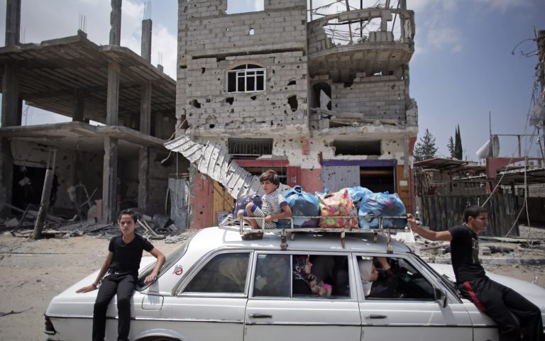 Palestinians in a car with their belongings drive past a destroyed house in Rafah's district of Shawkah in the southern Gaza Strip, Tuesday, Aug. 5, 2014. The attack at the Shawkah district east of the Gaza town of Rafah drew what was by far the heaviest shelling by the Israeli military in the Gaza war, killing nearly 100 people that day alone and instantly unraveling a three-day ceasefire shortly after it came into force. (AP Photo/Khalil Hamra)