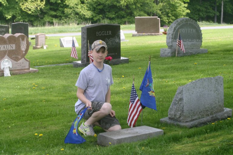In this May 27, 2013 photo provided by the New York State Troopers Police Benevolent Association, Darren Johnstone, the son of Trooper Stephen Johnstone, Troop F, places flags on the grave of Richard A. Van Alstyne  at Laurel Hills Cemetery in White Sulphur Springs, N.Y., on Memorial Day.  Van Alstyne, who died in 1977, served as a New York State Trooper for 20 years and was one of the last members assigned to the motorcycle patrol in Sullivan County, N.Y. Johnstone was participating in a program to honor and mark the graves of every state trooper. (AP Photo/New York State Troopers Police Benevolent Association)