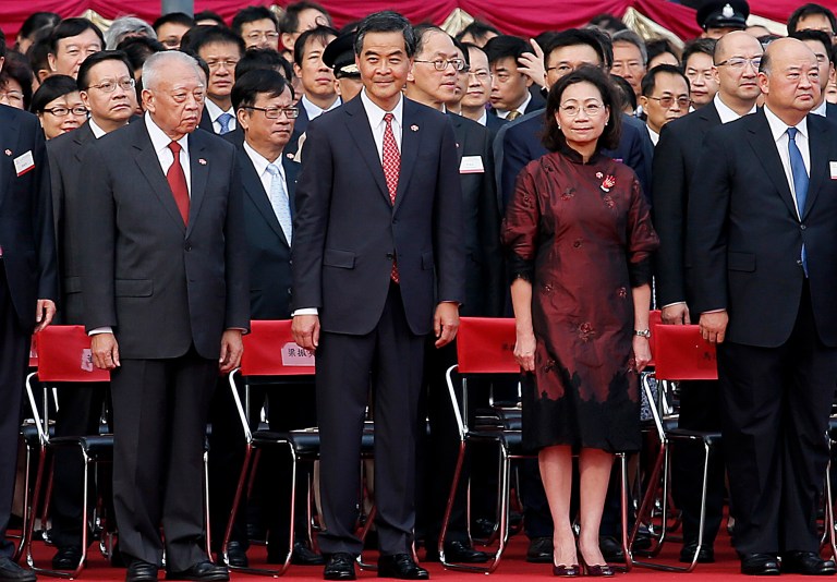 FILE - in this Oct. 1, 2014 file photo, Hong Kong's Chief Executive Leung Chun-ying, center, stands when the national anthem of China is played during a flag-raising ceremony  in Hong Kong, as thousands of protesters watching from behind police barricades yelled at him to step down.  The story Leung,  Hong Kong's top leader, is a rags-to-riches tale that is generally admired in this commercially-minded city. But Leung is deeply unpopular, thanks mainly to his longstanding ties with mainland China.  Beijing's burgeoning influence in this former British colony is a key factor driving protests that have paralyzed parts of this dynamic city and brought on some of the worst confrontations in decades. (AP Photo/Wong Maye-E, File)
