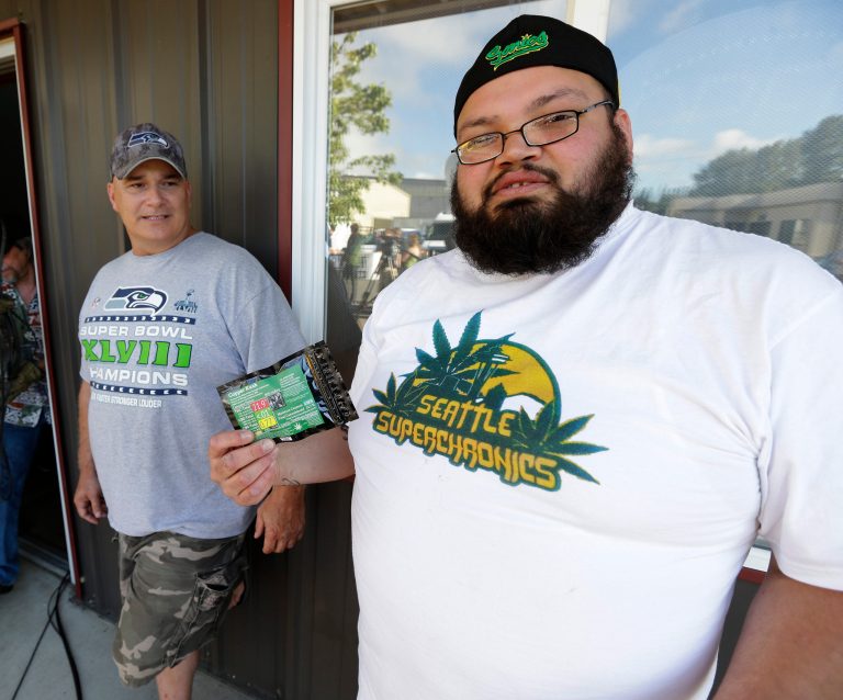Julian Rodriguez, right, of Everson, Wash., holds his two-gram packet of recreational marijuana outside Top Shelf Cannabis, Tuesday, July 8, 2014, in Bellingham, Wash., on the first day of legal sales. At left is Tom Beckley, the owner of the store. (AP Photo/Ted S. Warren)