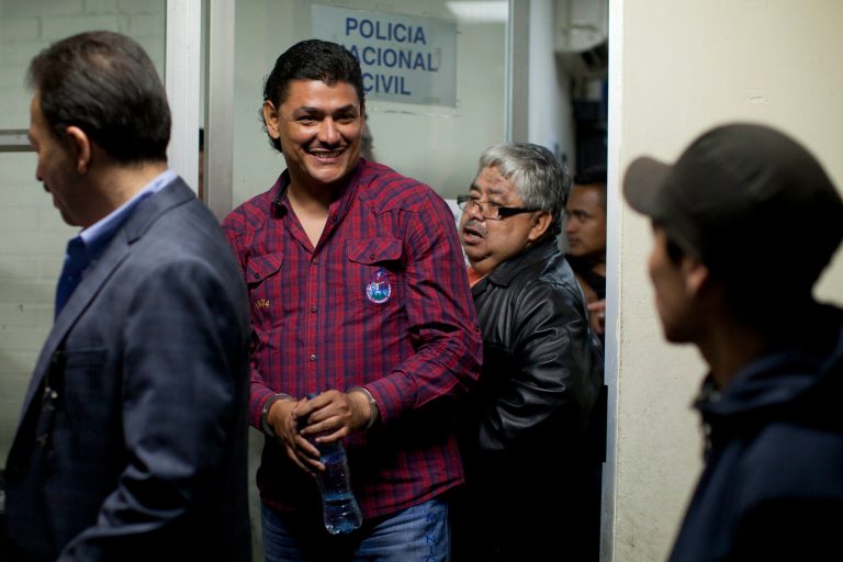 Handcuffed radio host Marlon Puente Rimula, second from left, smiles as he is escorted by police to a courtroom, in Guatemala City, late Tuesday night, May 13, 2014. Guatemalan police arrested the radio host who leads a fan organization for the Club Municipal soccer team for allegedly inciting fellow fans to kill a supporter of a rival team. Puente Rimola and two other men were arrested for the April 27 beating and stabbing death of Kevin Diaz, a 17-year-old fan of the rival team, Comunicaciones. (AP Photo/Moises Castillo)