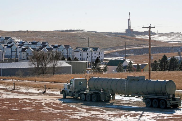 In this Wednesday, Feb. 26, 2014 photo, an oil truck sits in a dirt lot near a new housing development in Watford City, N.D. The housing development is part of the towns growth explosion from the Baaken oil boom. For years, the town's population hovered around 1,500. Now its at about 7,000 - a number that's expected to more than double in years to come. (AP Photo/Martha Irvine)