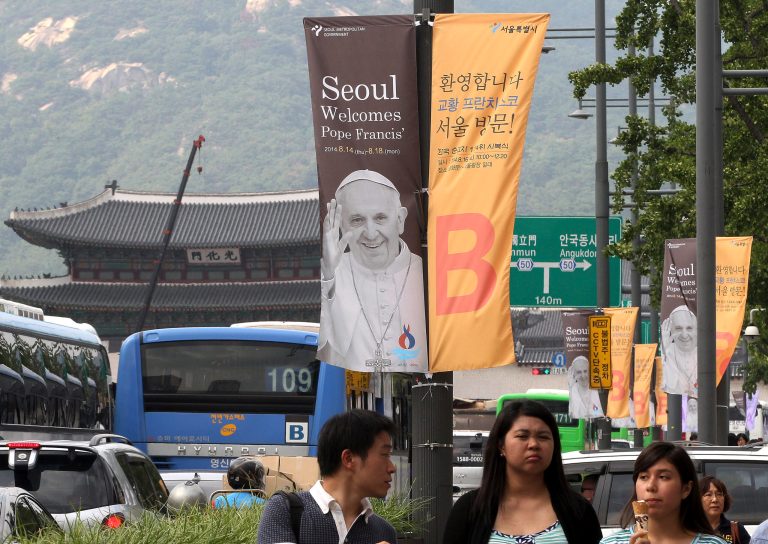 People walk past banners welcoming Pope Francis on the street in Seoul, South Korea, Monday, Aug. 11, 2014.  Pope Francis is scheduled to make a five-day trip to South Korea, starting Aug. 14 to participate in a Catholic youth festival and to preside over a beatification ceremony for 124 Korean martyrs. (AP Photo/Ahn Young-joon)