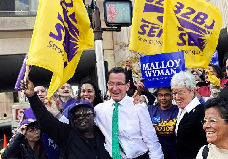 Members of 32BJ SEIU, property service workers union, stand with Gov. Dannel P. Malloy, center, before a debate between Malloy and Republican candidate Tom Foley, Thursday, Oct. 9, 2014, in Hartford, Conn.  Organized labor is devoting millions of dollars and countless man-hours to re-elect Gov. Dannel P. Malloy, a Democrat considered an important ally of unions despite a 2011 clash with unionized state employees in which he threatened massive layoffs during a budget impasse. (AP Photo/Jessica Hill)