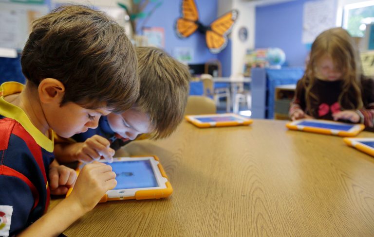 In this Thursday, Sept. 18, 2014 photo, Aiden Crott, 7, center, helps Daniel Hernadez, 5, with his ScratchJr iPad program while Talia Levitt, 7, right, works with hers at the Eliot-Pearson Children's School in Medford, Mass. Researchers created the app that teaches basic computer programming to kindergartners. (AP Photo/Stephan Savoia)