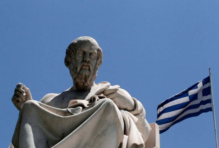   FILE- In this June 5, 2012, file photo, the marble statue of ancient Greek philosopher Plato, stands in front of the Athens Academy, as the Greek flag flies in Athens. Bankers, governments and investors are starting to prepare for Greece to drop the euro currency, a move that could spread turmoil throughout the global financial system. A Greek election on Sunday, June 12, 2012, will go a long way toward determining whether it happens. (AP Photo/Dimitri Messinis, File)  