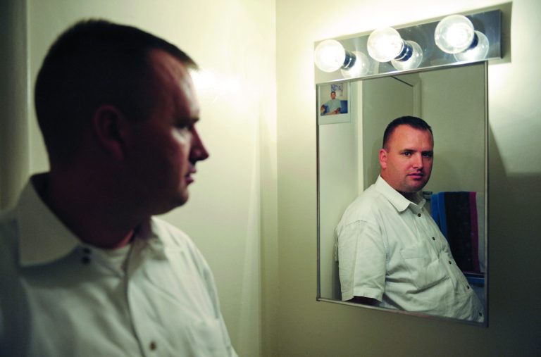 In this Aug. 23, 2012 photo, Kevin Earley, 33, stands next to the medicine cabinet which has an old photo taped to it, in the bathroom of his Vienna, Va., apartment that he shares with a roommate. 